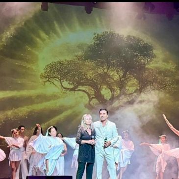 Performers on stage with a tree and sun backdrop.