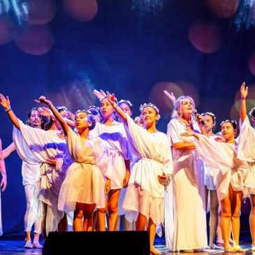 Group of performers in white costumes on stage.