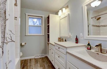 Bright bathroom with white cabinetry and wood flooring.