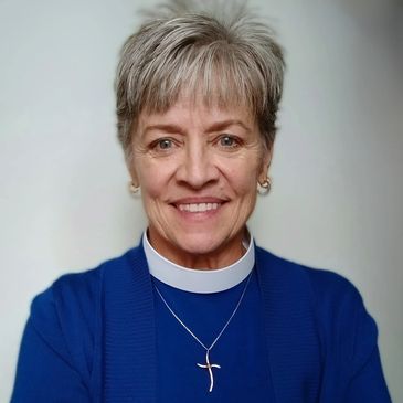 Smiling woman wearing a clerical collar and a cross necklace.