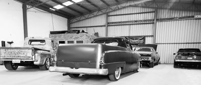 Black and white image of classic pickup trucks and cars in a garage.