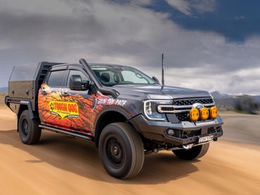 Black Ford pickup truck with Tough Dog 4WD suspension driving on a dirt road.