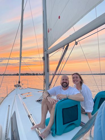 Couple sitting on sailboat and smiling at sunset
