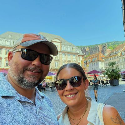 Couple smiling outdoors in a European city square with historic buildings.