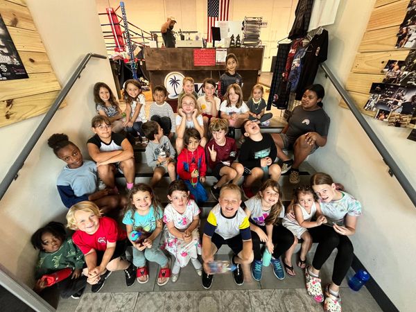 A diverse group of children sitting together on stairs in a gym setting.