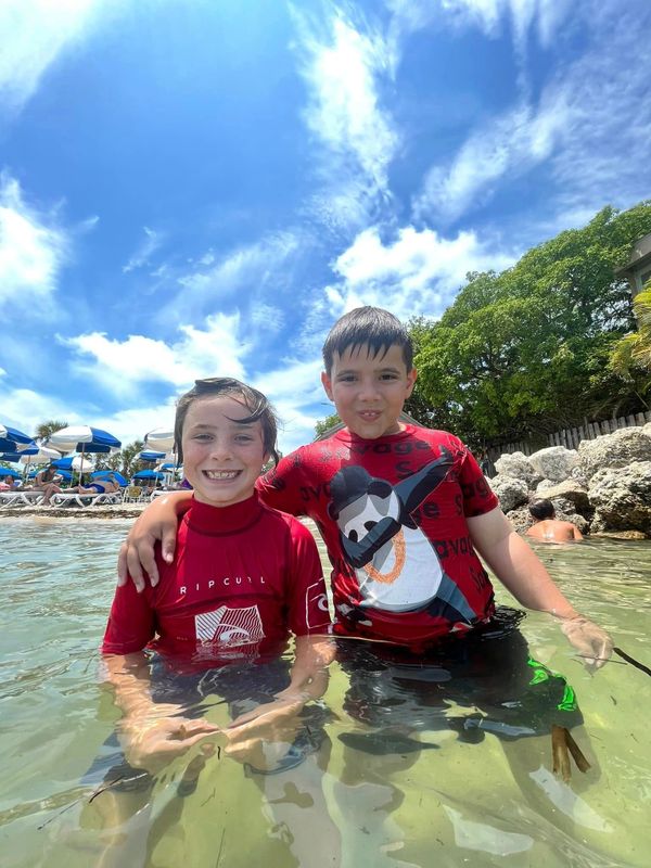 Two boys smiling and enjoying water at the beach on a sunny day.