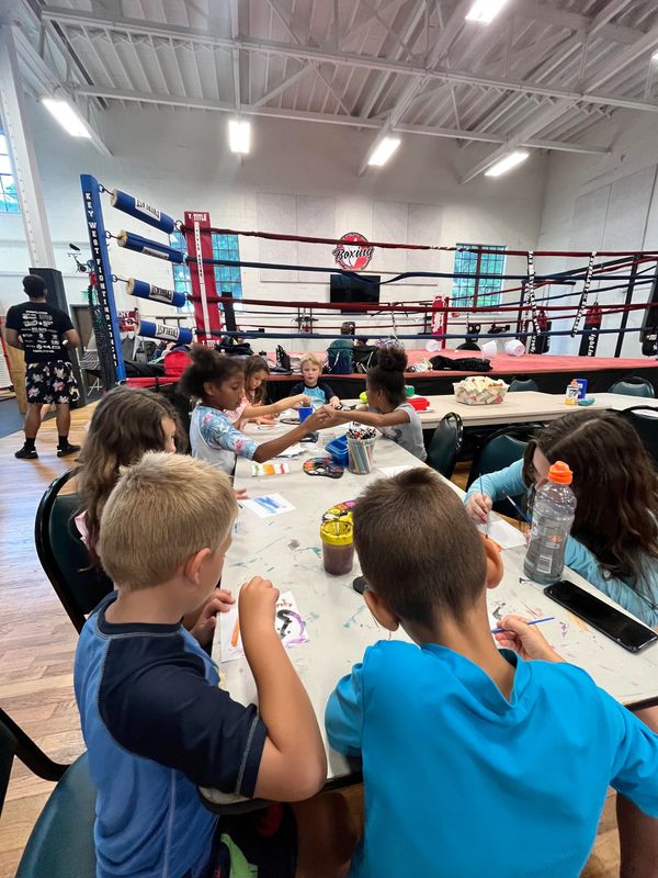 Children painting and crafting at a table in a boxing gym.