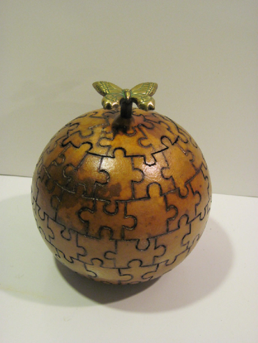 A round gourd that looks like it was made out of puzzle pieces with a butterfly on the lid.