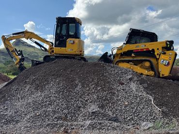 Two yellow CAT construction machines on a gravel mound under a cloudy sky.