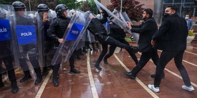 Protesters confront riot police with shields on a rainy day.