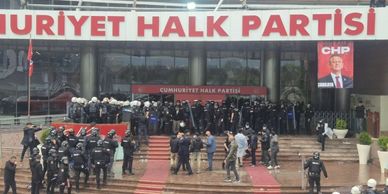 Police officers stand guard outside Cumhuriyet Halk Partisi building with banners and posters visible.