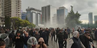 Crowd of people walking through a misty, urban area with tall buildings.