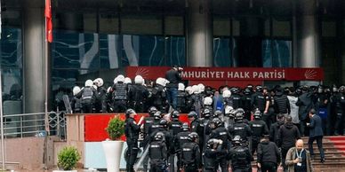 Police officers gather outside a building with a sign in Turkish.