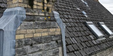 Stone chimney on a sloped tiled roof with skylights.