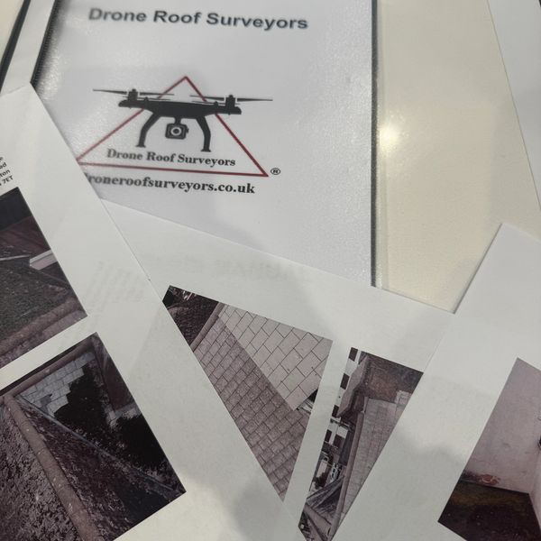 Documents and photos from Drone Roof Surveyors on a table.
