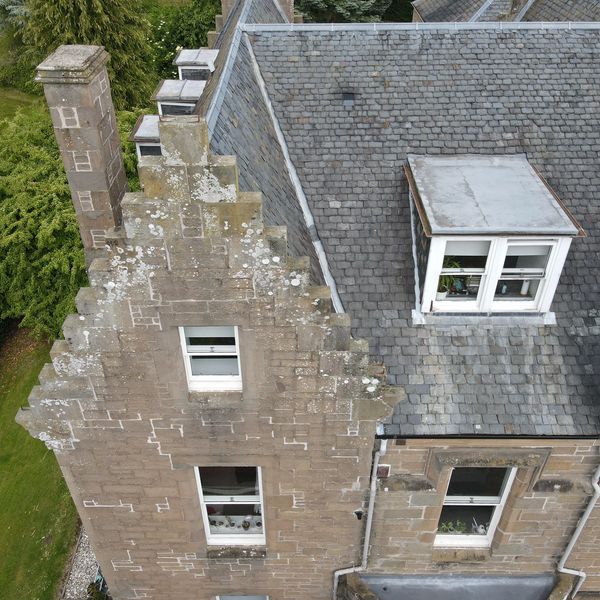 Aerial view of an old stone house with a slate roof and chimney.