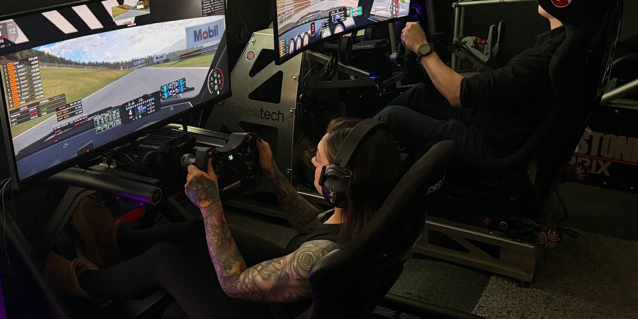 Two people racing on advanced driving simulators with large screens and steering wheels.