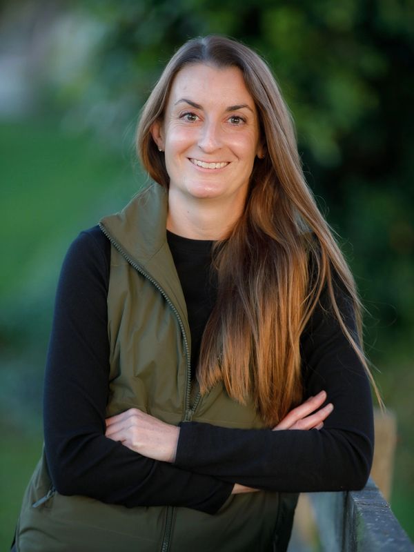 Smiling woman with long hair wearing a green vest and black shirt.