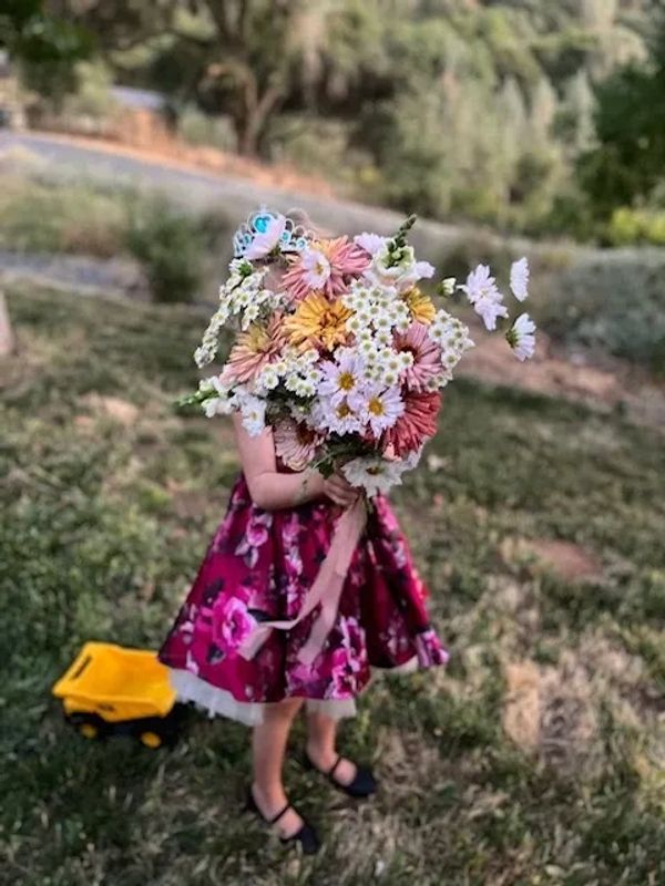 A child in a floral dress holding a large bouquet of colorful flowers outdoors.