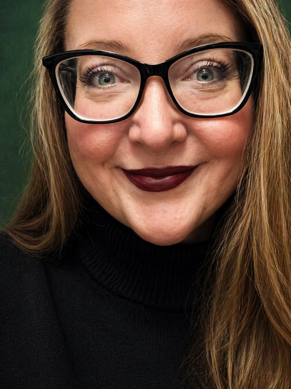 Photo of artist, Dannielle Vincent smiling wearing a black turtleneck and black cat eye glasses