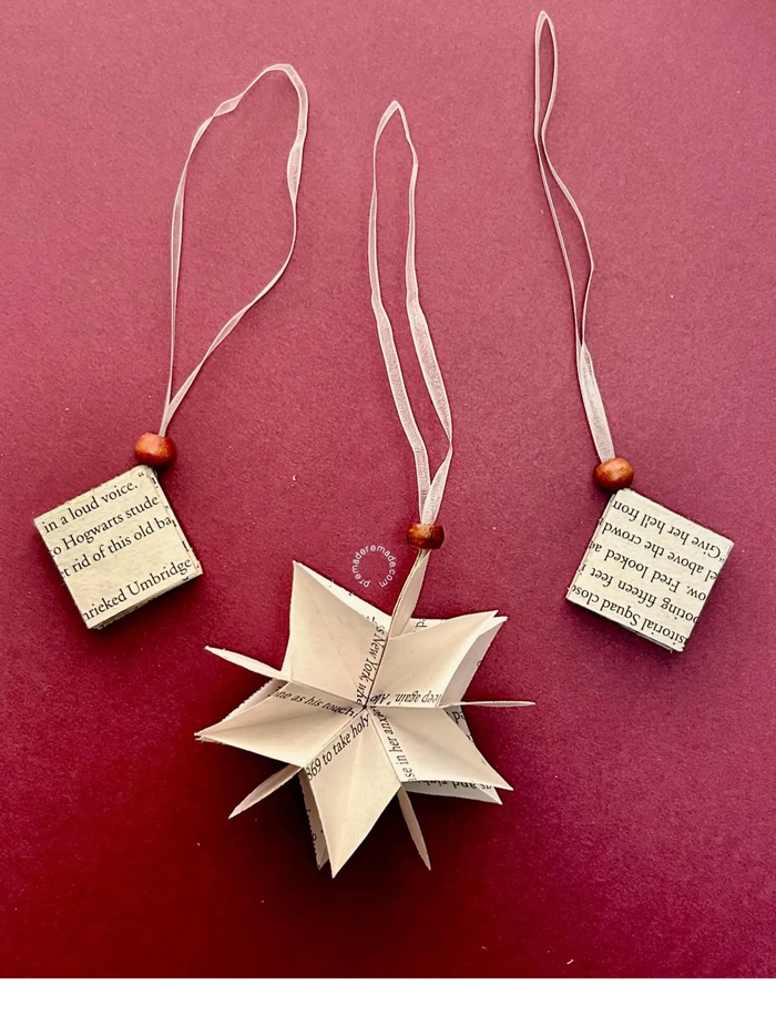 A bookish ornament with the pages folded to form a 3D five pointed star against a maroon background.