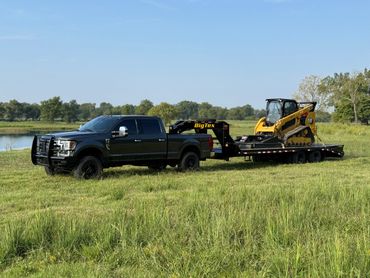 Black pickup truck towing a flatbed trailer with a yellow Caterpillar skid steer.