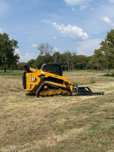 Yellow CAT compact track loader working on a grassy field under a blue sky.