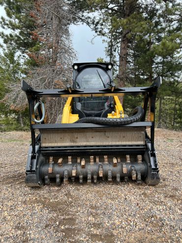 Front view of a yellow skid steer with a forestry mulcher attachment.