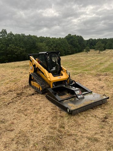 Yellow Caterpillar skid steer with a brush cutter attachment in a field.