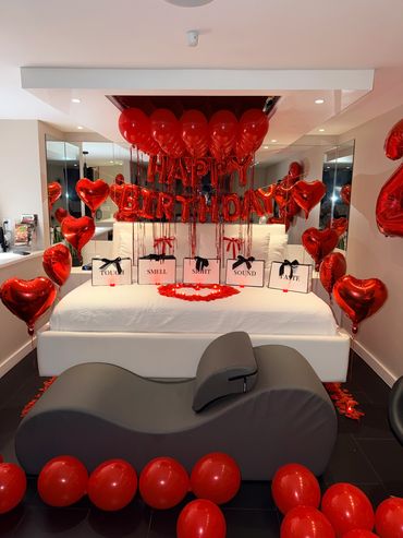 Red-themed birthday decoration setup on a bed with balloons and gifts.