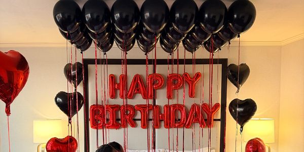 Red and black birthday balloon decorations on a bed headboard.
