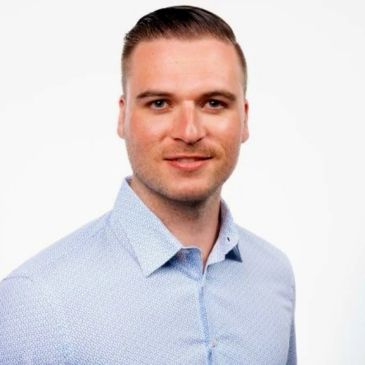 Man in a light blue patterned shirt smiling at the camera.