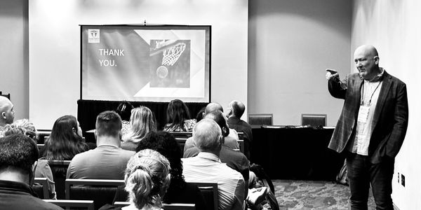 Speaker concludes presentation with a 'Thank You' slide in front of an audience.
