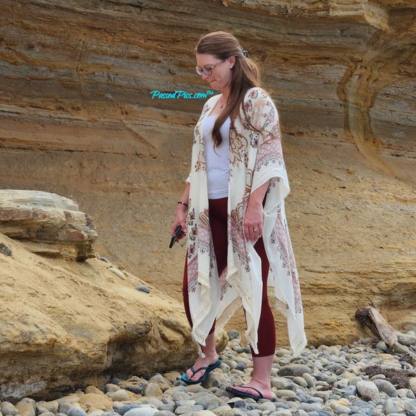 Beautiful married Lady on a pebble beach in a cave wearing a white shirt light shawl & flip flops