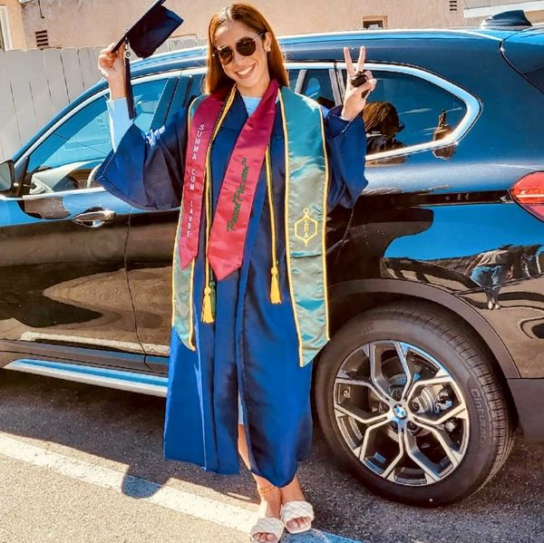 Beautiful lady wearing a Suma Cum Laude sash while tipping a graduation cap & holding the peace sign