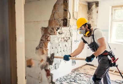 worker demolishing a wall with a sledgehammer wearing a protective mask