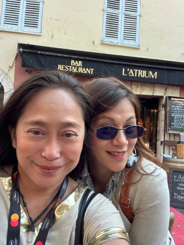 Two women smiling outside a restaurant called L'Atrium.