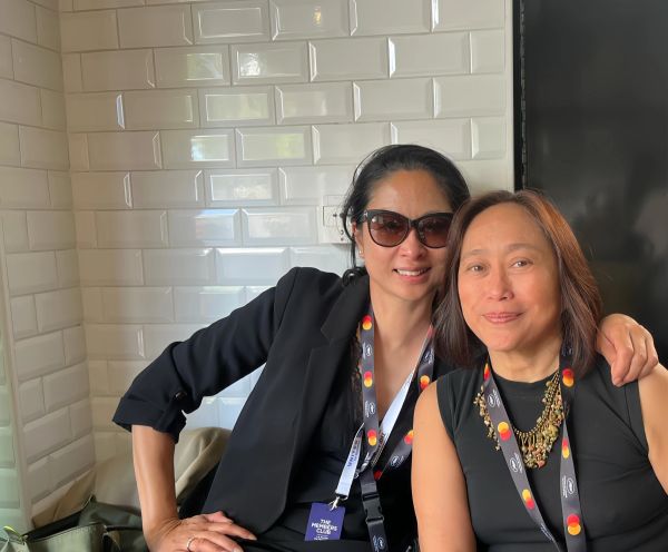 Two women sitting close, smiling, one wearing sunglasses.