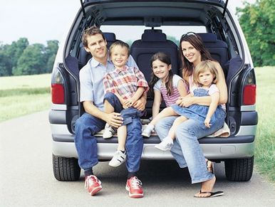 Happy family sitting at the back of their car outdoors.