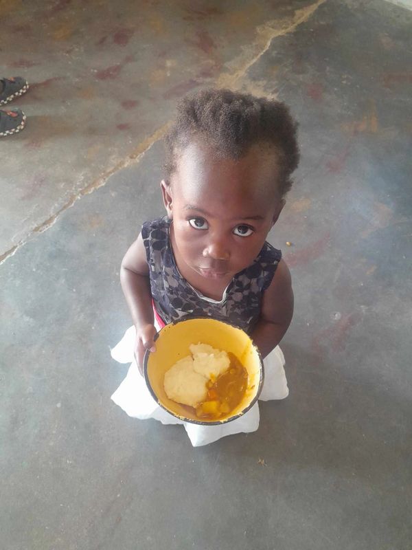 A little girl holding a yellow bowl with food, looking up.