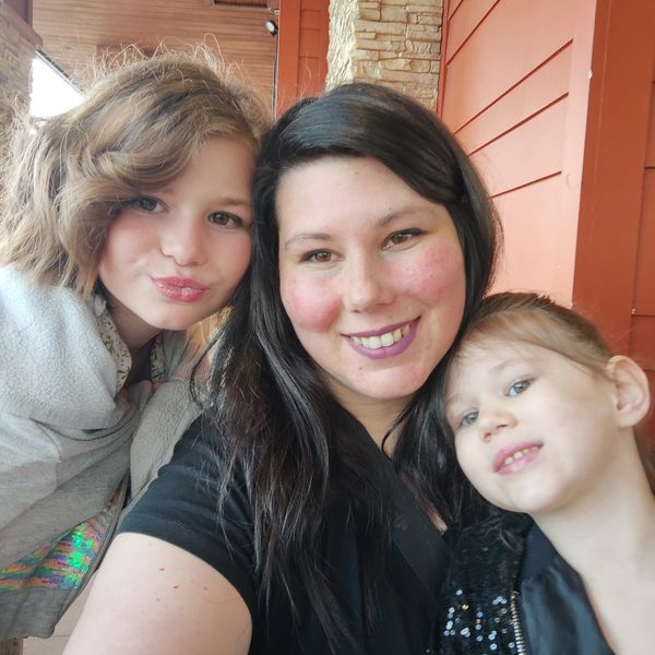 A smiling woman with two children posing for a selfie outdoors.