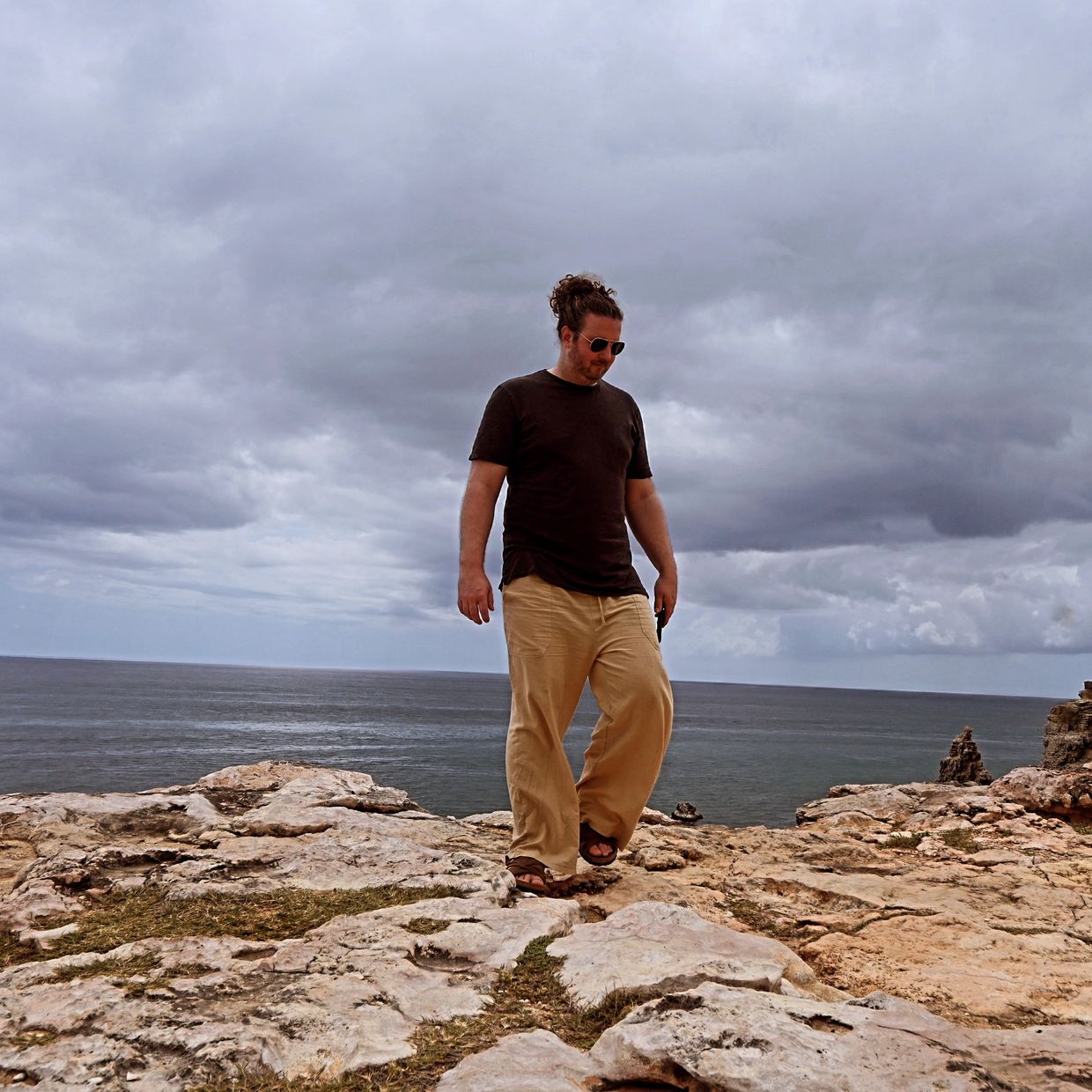 Man walking on rocky cliff by the ocean under cloudy sky.