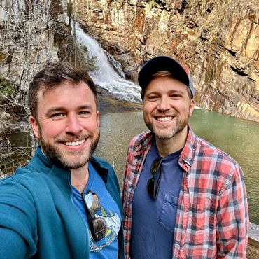 Husbands Todd and Rob smiling in front of a mountain waterfall at Tallulah Gorge State Park Georgia