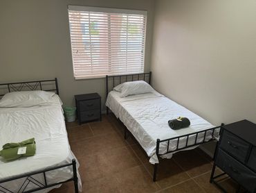 A simple bedroom with two single beds, each with a rolled green blanket.