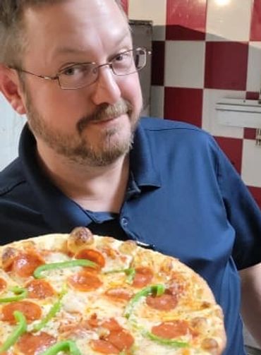 Manager Wes holding a made-to-order brick oven pizza in the kitchen at Rooster's Bar and Grill.