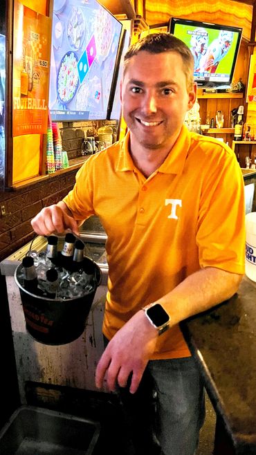 Employee at Rooster's Bar & Grill holding a bucket of beer bottles filled with ice behind the bar.