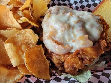 Fried chicken sandwich with cheese and toppings next to homemade potato chips in a basket.