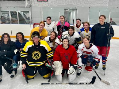 Group of female hockey players posing on ice rink in their gear.