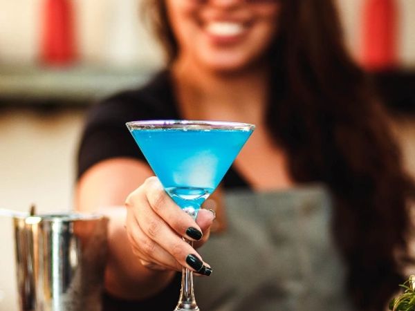 Woman holding a vibrant blue cocktail in a martini glass.