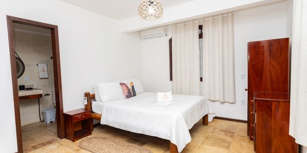 Minimalist bedroom with white bedding, wooden furniture, and an ensuite bathroom.